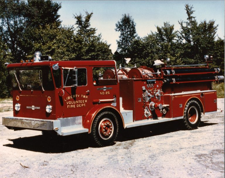 A vintage red fire truck from the Liberty Township Volunteer Fire Department is parked outdoors on a sunny day, proudly displaying its heritage against a backdrop of trees and blue sky.