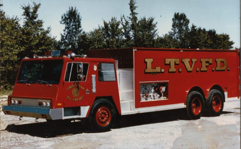 A red fire truck with "L.T.V.F.D." on the side and "Liberty Twp Vol. Fire Dept." on the door, representing the Liberty Township Volunteer Fire Department, is parked on gravel with trees in the background.