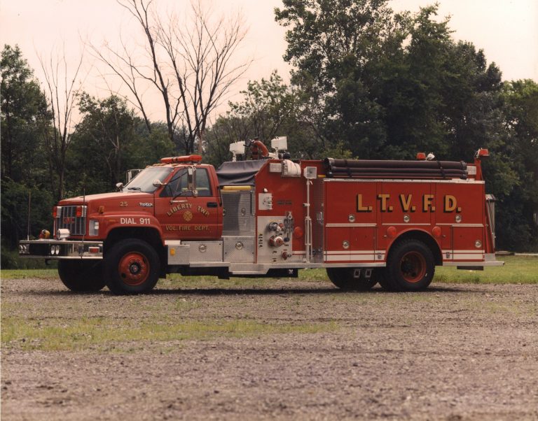 A red fire truck labeled "L.T.V.F.D." and "Liberty Twp. Vol. Fire Dept." from the Liberty Township Volunteer Fire Department is parked on a gravel lot, surrounded by trees and greenery in the background.