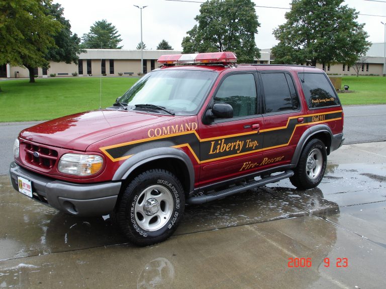 A red Liberty Township Fire Rescue command SUV with emergency lights is parked on wet pavement near grass and trees, with buildings in the background.