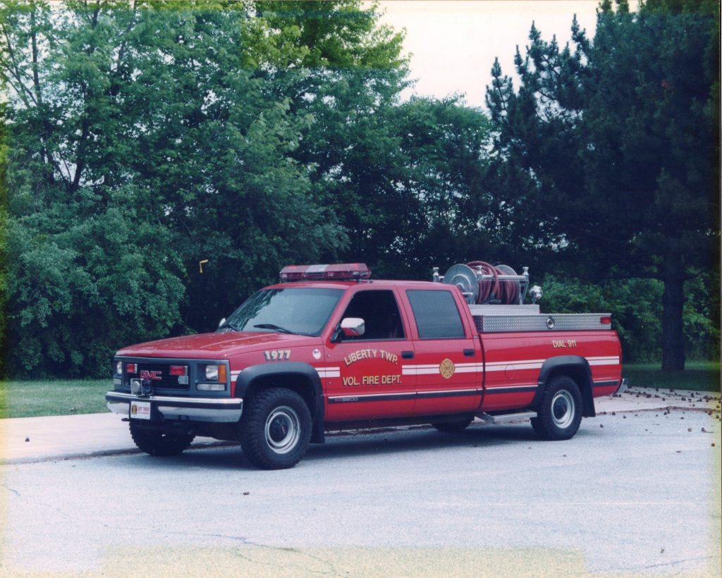 A red Liberty Township Volunteer Fire Department pickup truck is parked on a paved surface surrounded by green trees, with firefighting equipment from the department visible in the truck bed.