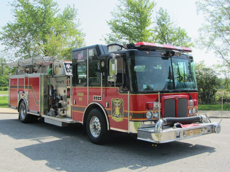 A red fire truck with silver accents and yellow detailing from the Liberty Township Volunteer Fire Department is parked on a paved surface near green trees and grass on a sunny day.