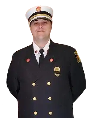 A person wearing a formal Liberty Township Volunteer Fire Department fire chief uniform, with a white hat, dark jacket adorned with badges and gold buttons, stands with hands behind their back, facing the camera.