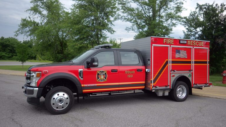A red Liberty Township Volunteer Fire Department rescue truck with "Squad 1951" and an American flag on the side is parked on a paved road, surrounded by trees and greenery.