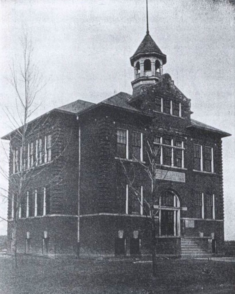 Black and white photo of a two-story brick school building with a central entrance, large windows, and a small bell tower—once used by the Liberty Township Volunteer Fire Department. Leafless trees are visible in the foreground.